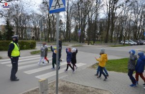 Policjant stoi przy przejściu dla pieszych. Po pasach przechodzą dzieci.