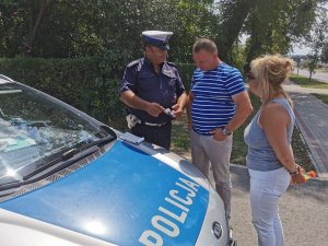 policjant wręcza ulotkę małżeństwu na poboczu drogi