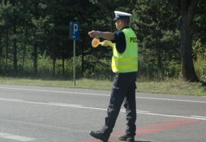 Policjant Wydziału Ruchu Drogowego w kamizelce odblaskowej kierujący ruchem.