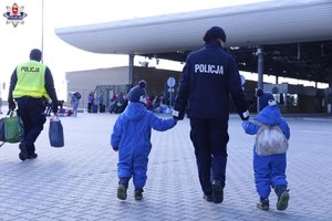 Policjantka prowadzi dwoje dzieci na przejściu granicznym