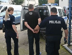 Dwoje policjantów w umundurowaniu służbowym doprowadza do Prokuratury sprawcę kradzieży rozbójniczej, który ma założone kajdanki na ręce trzymane z tyłu