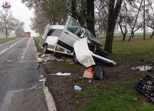 zniszczony w wyniku wypadku biały bus stojący koło drzew