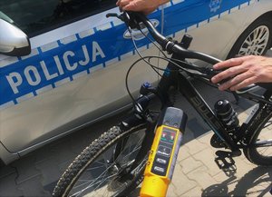 Rower stojący obok policyjnego radiowozu. Na pierwszym planie widoczne urządzenie do pomiaru stanu trzeźwości