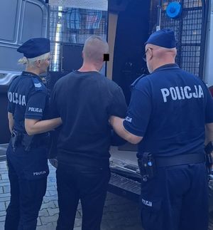 umundurowani policjanci stojący przy radiowozie służbowym z zatrzymanym