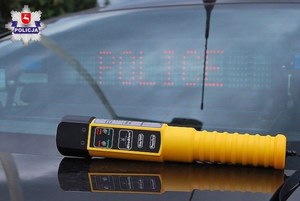 urządzenie służące do pomiaru stanu trzeźwości leżące na masce samochodu. w tle napis policja.
