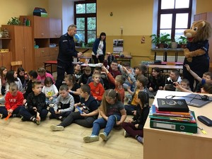 umundurowany policjant rozdaje odblaski w grupie dzieci