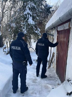umundurowani policjanci idą po śniegu w pobliżu zabudowań