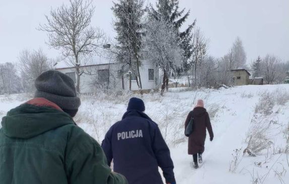 policjant z pracownikami opieki społecznej idzie przez zaśnieżoną ścieżkę do domu mieszkalnego