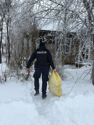umundurowany policjant idzie do domu z siatką z zakupami
