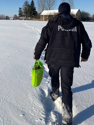 umundurowany policjant idzie zaśnieżoną ścieżką z torbą z zakupami