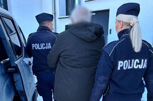 umundurowani policjanci prowadzą zatrzymanego mężczyznę do samochodu