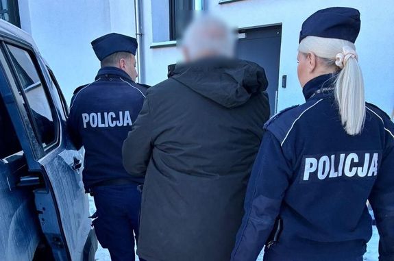 umundurowani policjanci prowadzą zatrzymanego mężczyznę do samochodu