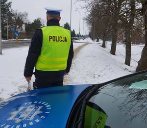 Na zdjęciu uwidoczniono umundurowanego policjanta drogówki, który stoi przy oznakowanym radiowozie