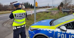 Umundurowany policjant wydziału ruchu drogowego stoi przy oznakowanym radiowozie