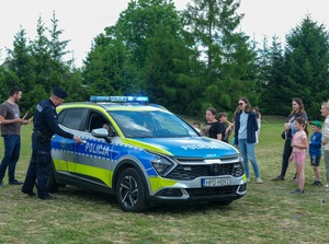 radiowóz, w środku dzieci, obok stoi umundurowany policjant
