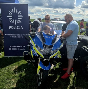 motocykl policyjny, na którym siedzi dziecko. Obok stoi mężczyzna z kobietą